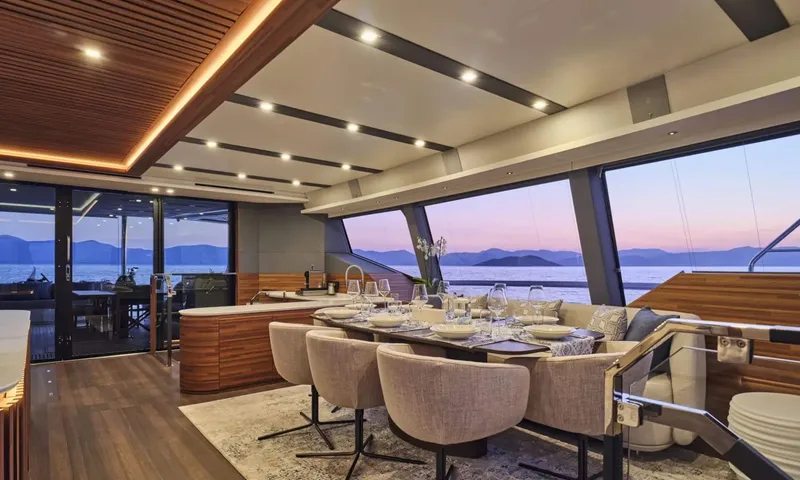 Alina: Set dining table with upholstered chairs beside panoramic windows overlooking the sea at sunset