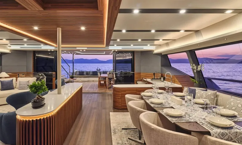 Alina: Interior dining table set for dinner with lounge and galley counter, glass doors open to aft deck