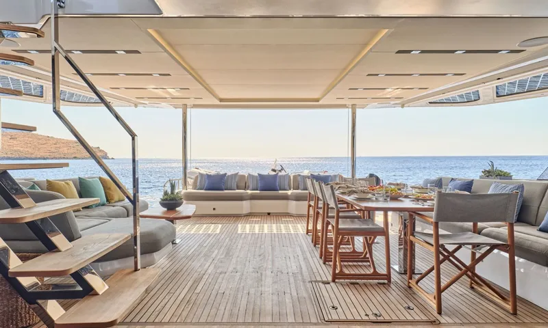 Alina: Shaded aft deck with teak floor, dining table set for a meal and cushioned sofas facing the sea