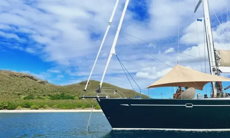 Crazy H: Bow of a dark hulled yacht with shade awning, anchored off a grassy island