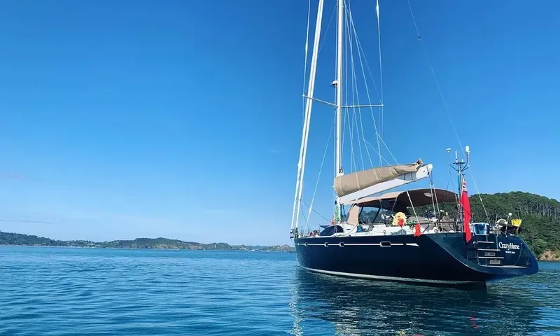 Crazy H: Dark blue hulled sailing yacht at anchor in a calm green bay under clear sky