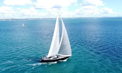 Crazy H: Sailing yacht under full white sails crossing open blue water, seen from above