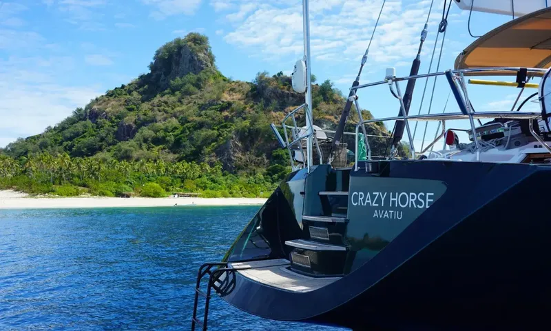 Crazy H: Stern with boarding steps and ladder near a tropical beach and green rocky hill
