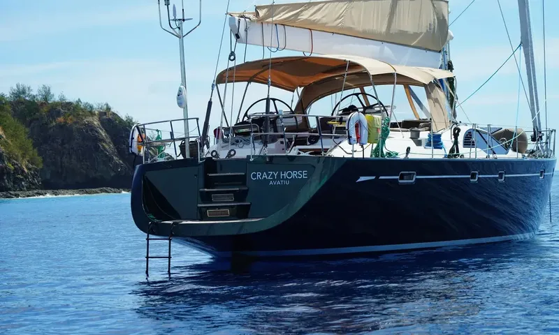 Crazy H: Stern quarter of a dark yacht with bimini cockpit and boarding ladder near rocky shore