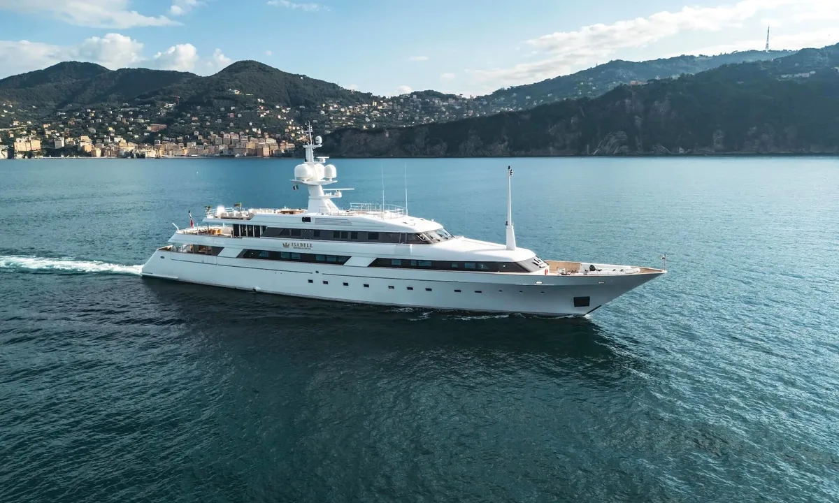 Isabell Princess of the Sea: White motor yacht cruising across calm blue water past a hillside coastal town, seen from above