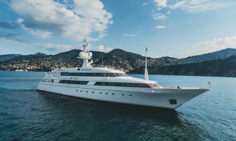 Isabell Princess of the Sea: White motor yacht under way near green hills and a coastal town under a partly cloudy sky