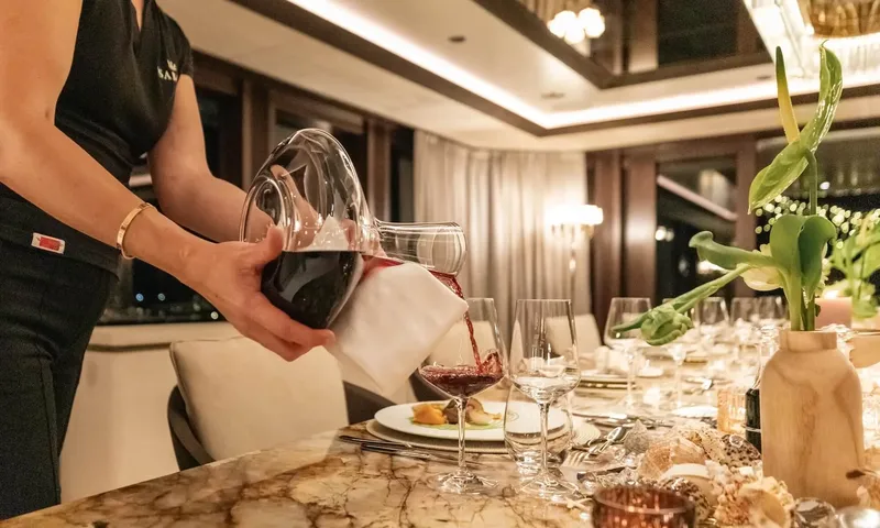 Isabell Princess of the Sea: Crew member pouring red wine from a decanter at a set indoor dining table