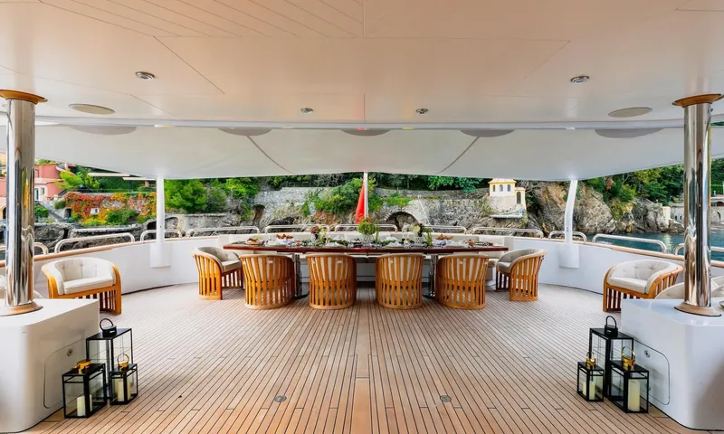 Isabell Princess of the Sea: Covered aft deck with long set dining table, wooden chairs and lanterns overlooking a rocky coast