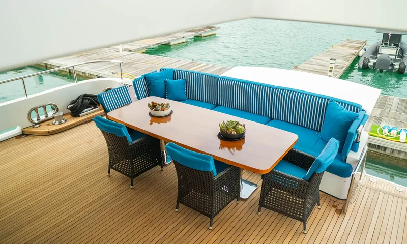 Indiana: Teak deck dining table with blue bench seating overlooking a pier and inflatable boat