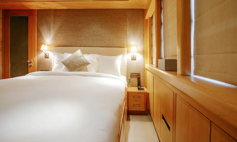 Indiana: Double bed with white linen between wall lamps, bedside drawers and wood cabinets