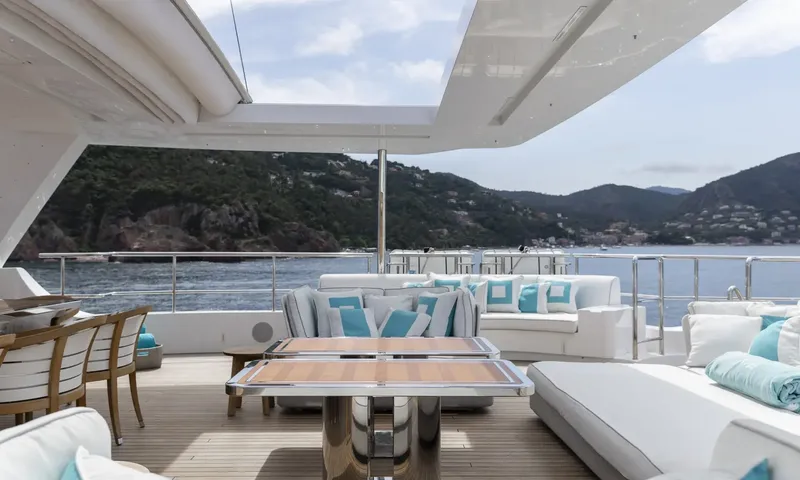 Nela: Outdoor lounge with white sofas, turquoise cushions and tables overlooking green hills and sea