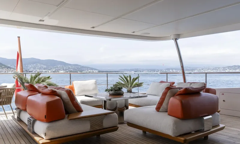 Nela: Shaded aft deck lounge with orange and white sofas facing the sea and hillside town