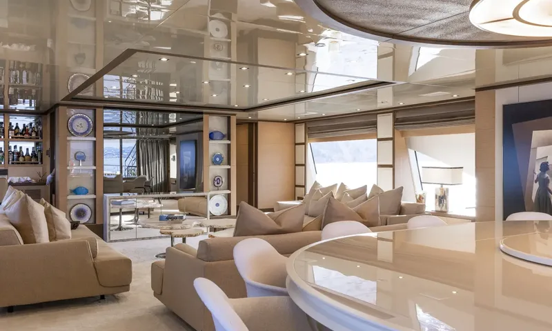 Nela: Open lounge with beige sofas, mirrored ceiling, display shelves and round dining table