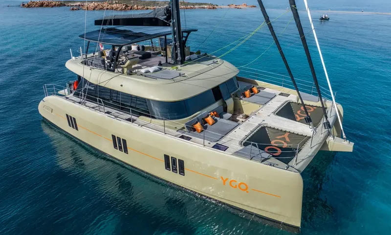 YGO: Elevated view of a catamaran at anchor in clear turquoise water near rocky shore