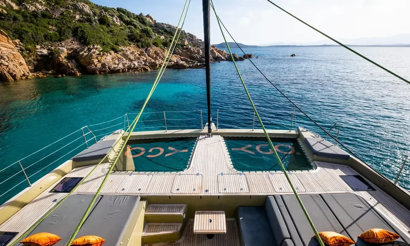 YGO: Foredeck lounge with cushions and trampoline nets facing a turquoise rocky cove