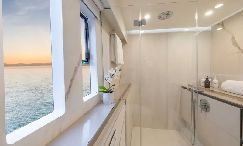 YGO: Bathroom with glass shower, marble walls and windows overlooking the sea at sunset
