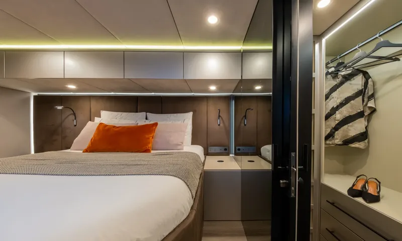 YGO: Double bed with orange cushion beside an open wardrobe with hanging clothes