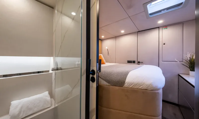 YGO: View from an ensuite shower into a cabin with a made bed and skylight