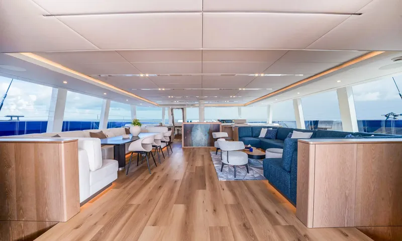 Hu-Lysse: Open main saloon with wood floor, dining table, blue lounge sofa and wraparound windows