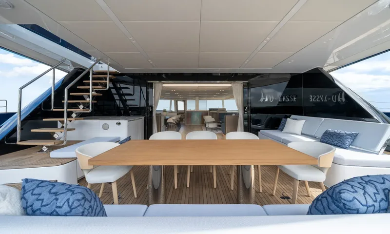 Hu-Lysse: Aft deck dining table with white chairs, cushioned sofas and view into the saloon