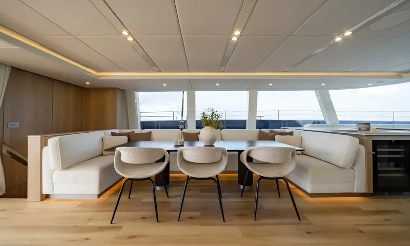 Hu-Lysse: Indoor dining table with curved white banquette and three upholstered chairs before large windows