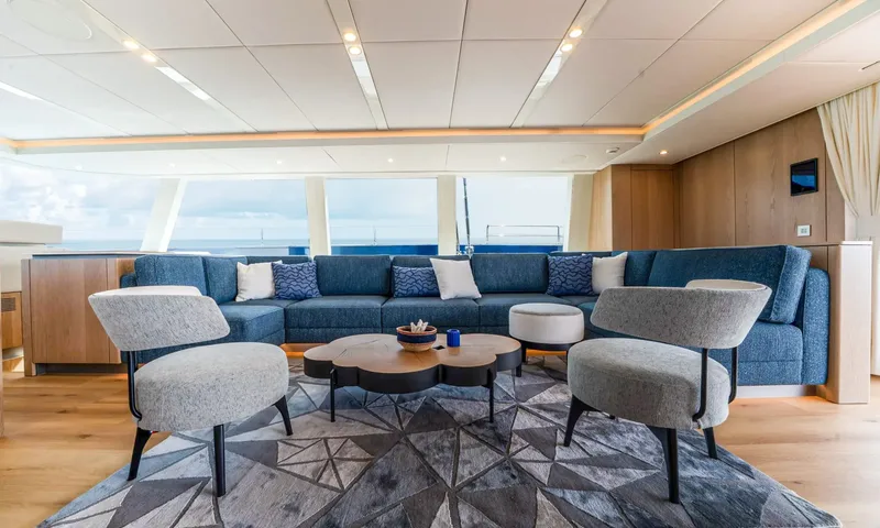 Hu-Lysse: Blue sectional sofa with two grey armchairs around a wooden coffee table on a geometric rug