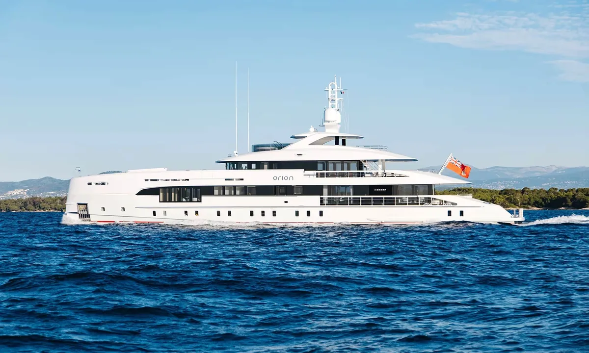 Orion: White motor yacht under way on deep blue sea with green hills behind