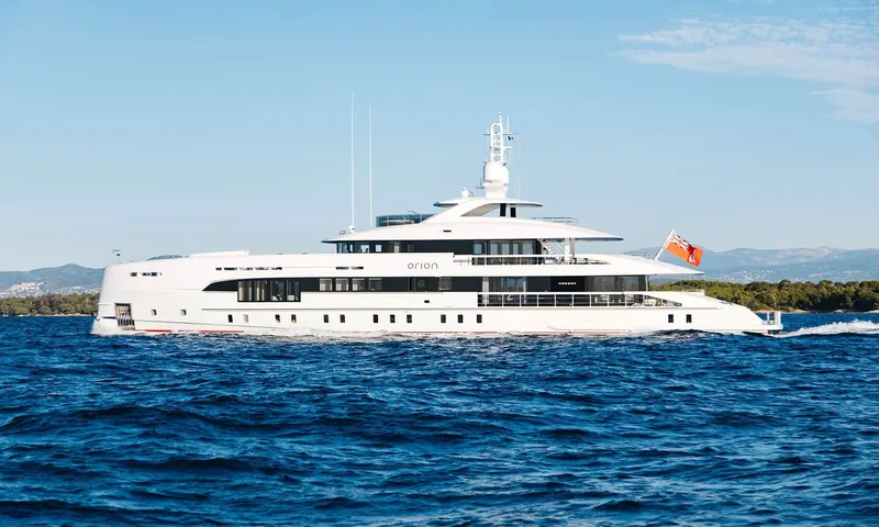 Orion: White motor yacht under way on deep blue sea with green hills behind