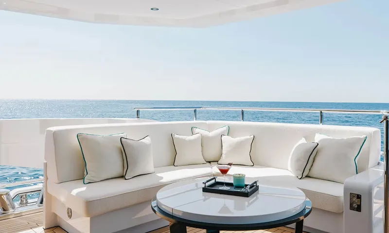 Orion: Curved white outdoor sofa with cushions and a round table holding cocktails by the sea