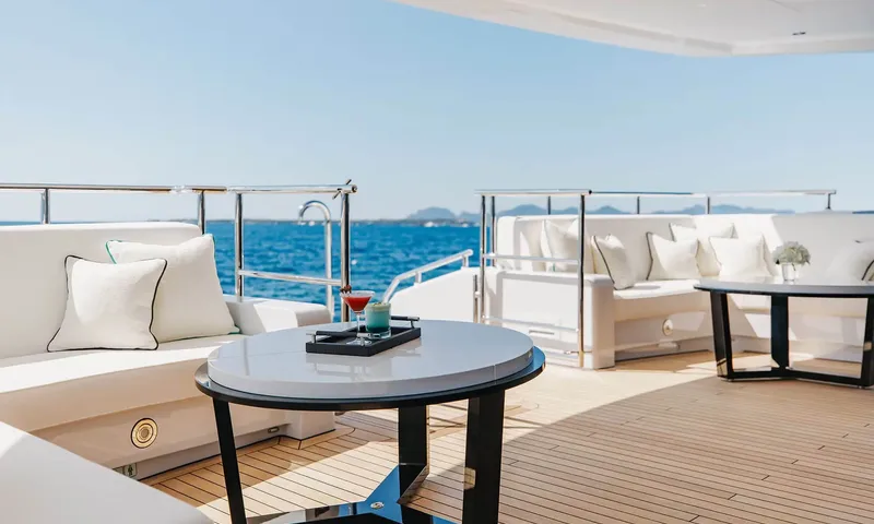 Orion: Aft deck seating with white sofas, round tables and drinks under a shaded overhang