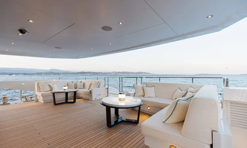 Orion: Covered teak deck with two white lounge areas and lanterns at dusk