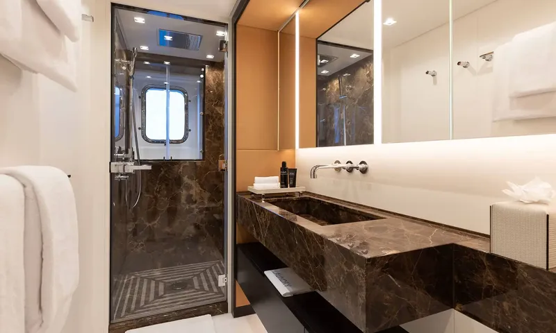 Orion: Bathroom with dark marble sink and glass shower with porthole