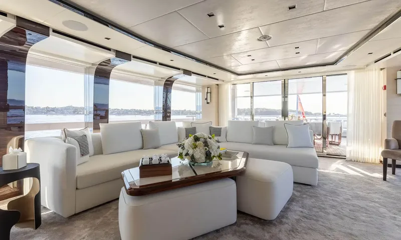 Orion: Saloon with white sectional sofa, ottomans and wide windows onto the coast