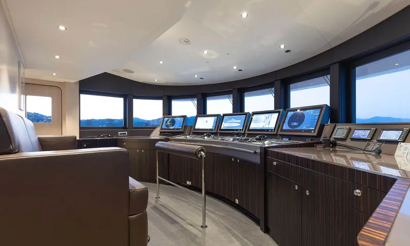 Orion: Wheelhouse with curved helm console, navigation screens, leather chair and panoramic windows at dusk