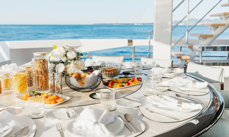 Orion: Round outdoor table set for breakfast with fruit, cereals and flowers beside the sea
