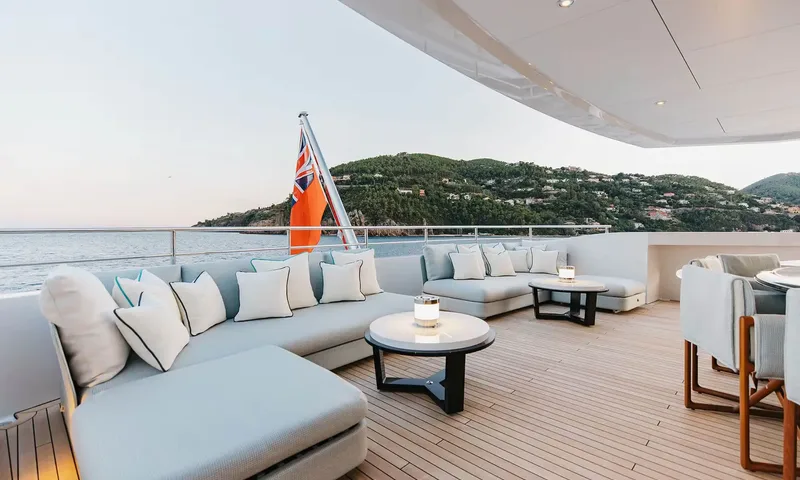 Orion: Aft deck lounge with corner sofas, cushions and coffee tables facing a green hillside
