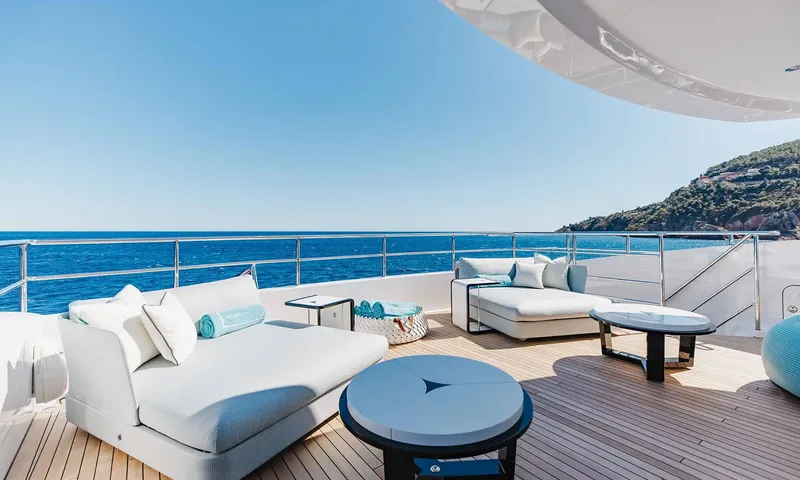 Orion: Shaded deck lounge with white daybeds and round tables overlooking the sea and a hillside