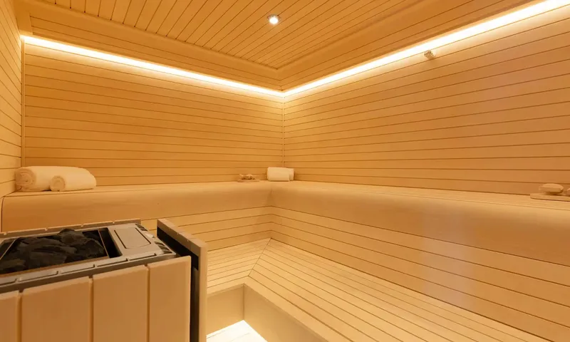 Orion: Wooden sauna with tiered benches, rolled towels, heater and soft ceiling lighting