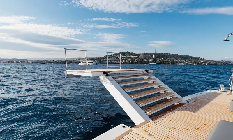 Orion: Folding stern platform with steps down to the sea and a coastal town beyond
