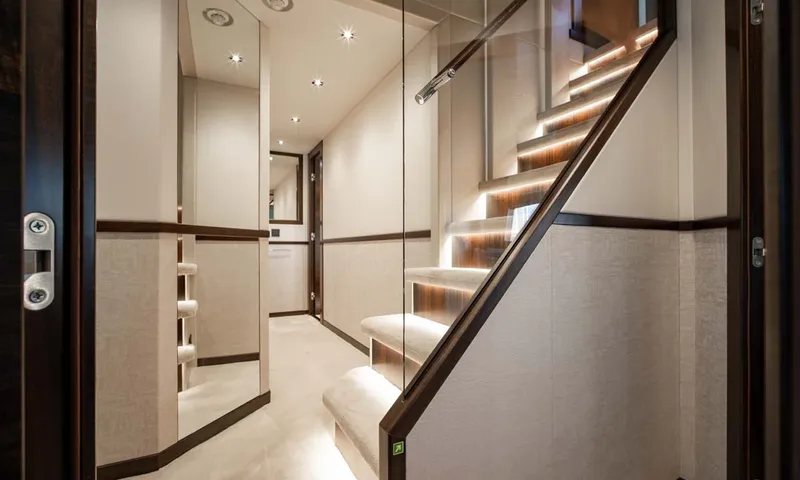 Nigora: Lower deck corridor with lit staircase and glass balustrade