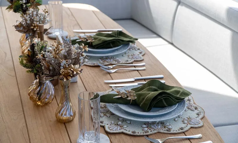 Nigora: Table setting with green napkins, beaded placemats and gold vases of dried flowers